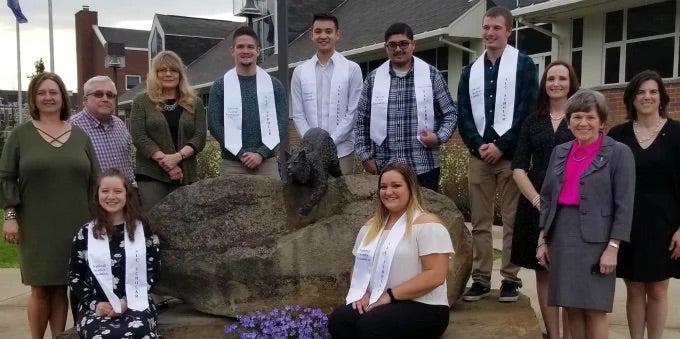 Twelve individuals (ten standing, two seated) posed with Bruiser the Bobcat statue.