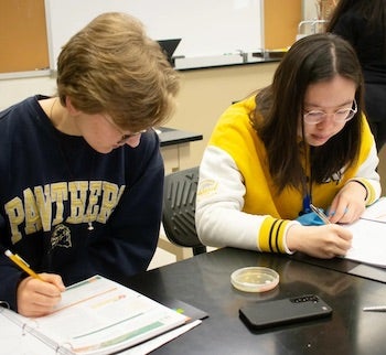 Two students seated, writing.